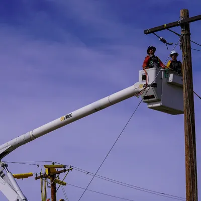 Two linemen in a bucket truck inspecting a distribution pole.